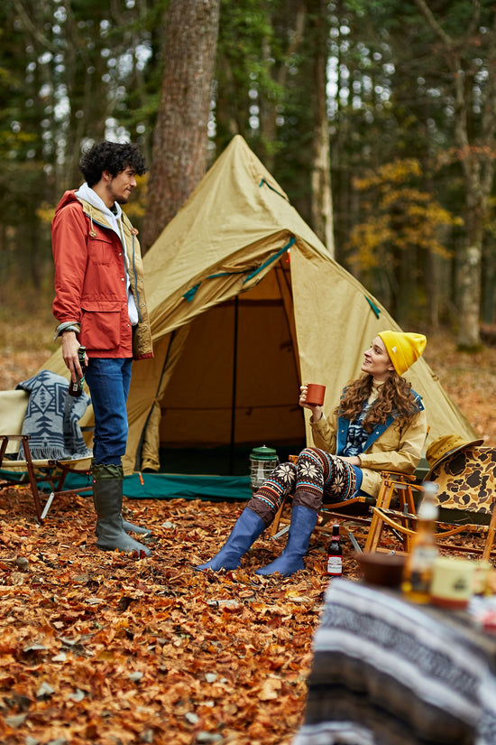 A guy and a lady out in the forest camping wearing their Pokeboo Packable Boots in Royal Blue and Charcoal colours