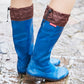 A person wearing royal blue Pokeboo  rain boots with brown waterproof cuffs, standing on wet stone pavement. A small red Pokeboo brand tag is visible on the side of the right boot.
