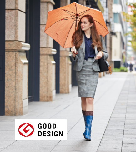 An image of a lady walking down an urban street wearing smart work clothes along with her Pokeboo Packable Boots in Royal Blue colour with the Good Design Award Winner logo being showcased.
