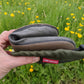 A hand holds a Pokeboo boot rolled up in their hand in front of a blurred field of yellow flowers. A red brand tag reading 'pokeboo' is visible on the pouch.