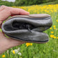 A close-up of a hand holding a rolled up Pokeboo boot in a grassy field with yellow flowers in the background.
