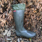 A single dark olive green/charcoal rubber rain boot with a matching green cuff, placed on a bed of dry brown leaves outdoors. A small red tag on the side of the boot shows the brand 'Pokeboo'.