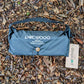A black blue Pokeboo Tread bag laid flat on a bed of brown wood chips and leaves, with its white brand tag attached.