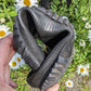 A hand holding a pair used Pokeboo TREADr ubber boots against a background of green foliage and white daisies.