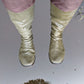 A pair of khaki Pokeboo rubber boots worn shown reflected in a puddle of water with trees visible at the bottom.