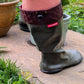 A person wearing khaki green Pokeboo TREAD rubber rain boots with a dark burgundy drawstring cuff, standing outdoors on a stone patio with potted plants in the background.